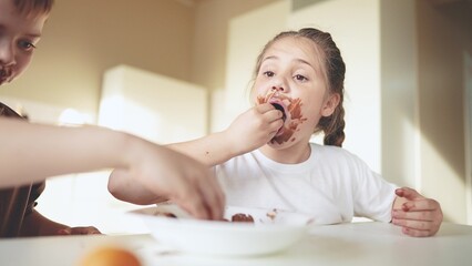 baby boy and girl eat chocolate. dirty little baby kids in the kitchen eating chocolate in the morni