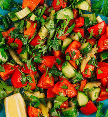 Fresh salad with chopped tomatoes, cucumbers, greens and herbs seasoned with oil and lemon juice