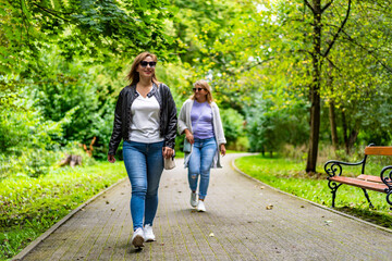 Wall Mural - Two women of european beauty in casual wears walking separately, one goes in front, other in back, in city park in early autumn.