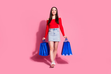 Wall Mural - Full body portrait of pretty young girl hold shop bags walk empty space isolated on pink color background