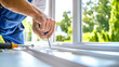 © Anoo - Close-up of a worker repairing plastic window frames from inside a bright kitchen with a view of a green garden on a sunny day