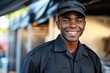 © Yuliia - Beautiful African American male security guard wearing a black uniform and a cap, smiling while providing service at an American event.