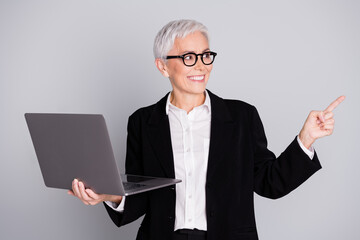 Sticker - Portrait of charming successful senior lady wear black stylish suit demonstrate promo empty space isolated on grey color background