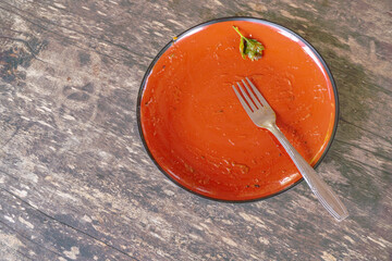 Empty Plate with Fork and Parsley. A close-up view of a clean, empty plate with a fork and parsley leaf resting on top. The plate has a red ceramic base and a black rim, suggesting it has been used fo