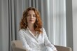 © Ева Поликарпова - A woman sits in a chair facing a window with a calm expression
