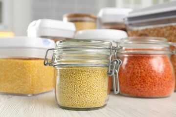 Sticker - Different types of cereals and legumes in containers on white wooden table, closeup