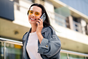 Wall Mural - Photo of cheerful pretty lady dressed grey jacket dark eyewear smiling communicating modern device outdoors town street