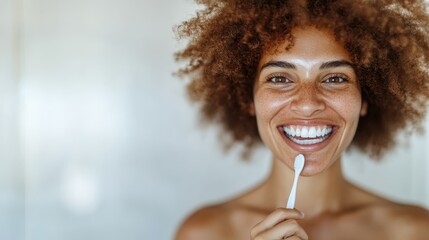 A cheerful woman with curly hair is brushing her teeth and smiling brightly. The image radiates positivity and good health, emphasizing her perfect dental hygiene.