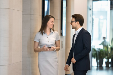 Poster - Positive couple of business colleagues talking, chatting in office hallway, walking together, smiling, laughing, keeping corporate network, communication. Business professional consulting coworker