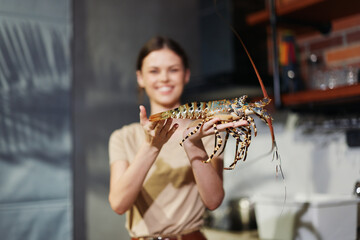 Wall Mural - Woman holding lobster in front of kitchen counter with red pots and pans