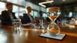 © Tanakrit - A close-up of an hourglass on a table, with blurred figures in the background, symbolizing time management and decision-making in a professional setting.