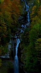 Wall Mural - Aerial view showcasing a majestic waterfall cascading down rocky mountains surrounded by lush greenery.