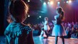 © Tanakrit - Young dancer watches other performers on stage, illuminated by colorful lights, capturing the magic of a dynamic dance showcase.