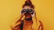 © Johannes - Woman looking through binoculars on yellow background.