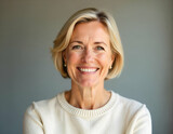 A smiling eldery woman Caucasian woman with short blonde hair wearing a cream-colored sweater