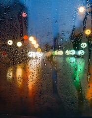 Wall Mural - Water drops on a glass with blurred city lights in the background