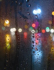 Wall Mural - Water drops on a glass with blurred city lights in the background