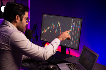 Smart trader businessman concentrating on dynamic stock exchange investment on pc and laptop showing on screen with high profit in searching market at neon light office in dark room night. Surmise.