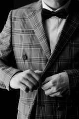 A man adjusting his plaid suit jacket before an evening event indoors at a formal setting