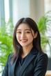© EarthWalker - Confident female business leader in black suit looking into camera in modern office with a green indoor plant. Portrait of beautiful smiling Asian businesswoman