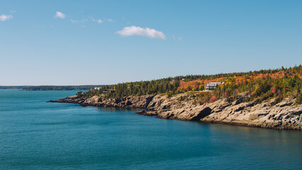 Wide View of Sand Beach Acadia National Park Lodge in Distance. Atlantic Ocean Blue with Rocky Shore and Colorful Trees in Autumn Maine New England