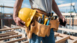© Hound - A man is holding a cell phone in his hand while wearing a yellow hard hat and a belt with tools