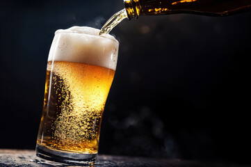 Poster - Cold beer pouring from bottle into glass with bubbles on black background