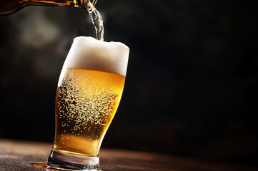 Poster - Cold beer being poured into glass on dark background