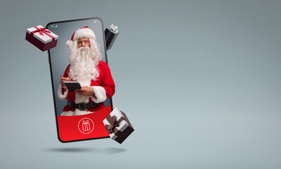 Wall Mural - Santa Claus in a smartphone screen and Christmas gifts