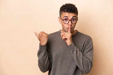 Wall Mural - Young Brazilian man isolated on beige background pointing to the side and doing silence gesture