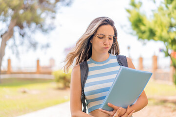 Poster - Young pretty student woman at outdoors with sad expression