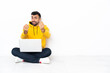 © luismolinero - Caucasian man sitting on the floor with his laptop making money gesture