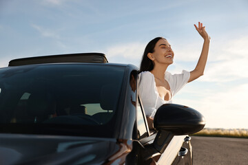 Canvas Print - Smiling young woman leaning out of car window outdoors. Enjoying trip