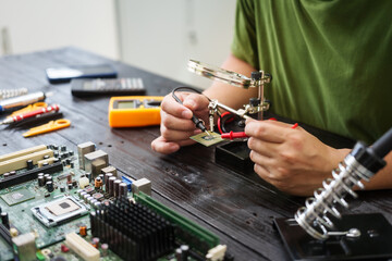 Technician carefully repairs a computer circuit board, using precision tools to address hardware issues. technical expertise needed for troubleshooting and upgrading electronic systems in workspace.