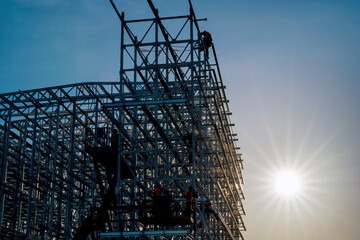 Workers working at height on clad rack structure installing steel elements of framework during sunny morning