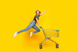 © deagreez - Full size photo of optimistic girl dressed khaki crop top ride on shopping cart to empty space isolated on yellow color background