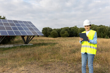 Happy Female Solar energy engineer or technician using a tablet to inspect a solar panel structure in a rural field