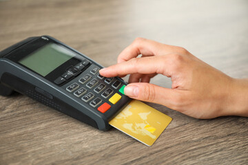 Canvas Print - Woman with credit card using payment terminal at wooden table indoors, closeup