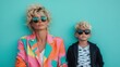 © svastix - A mother with tousled hair in a vibrant multi-colored outfit sitting next to her child, who wears a striped shirt and jacket, both against a solid teal-colored wall backdrop.