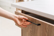 © brizmaker - Hand reaching to open a wooden drawer with a black handle in a modern kitchen