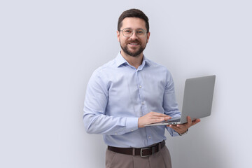 Wall Mural - Portrait of smiling businessman with laptop on grey background