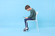 © New Africa - Boy with incorrect posture and phone sitting on chair against light blue background