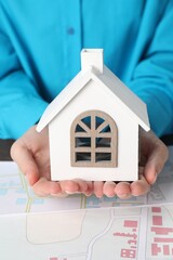 Wall Mural - House hunting. Woman with maps and house figure at wooden table, closeup