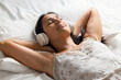 © nenetus - Beautiful young woman listening to music with headphones while relaxing lying on the bed at home