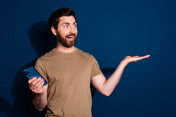 Poster - Photo portrait of young guy model in beige t shirt using smartphone demonstrate ebanking isolated on dark blue color background