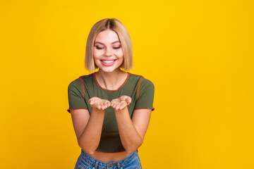 Wall Mural - Photo of appreciative girl with bob hair dressed khaki t-shirt look at object on palms empty space isolated on yellow color background