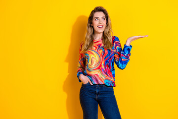 Poster - Photo of young shocked funky woman wearing colorful pullover and hold arm looking great deal isolated on yellow color background