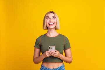 Poster - Photo of clever girl with bob hairdo dressed khaki crop top hold smartphone look at logo empty space isolated on yellow color background