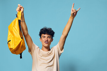 Young man celebrating with raised hands and a backpack against a bright blue background, showing excitement and enthusiasm A playful expression captures a moment of joy and freedom