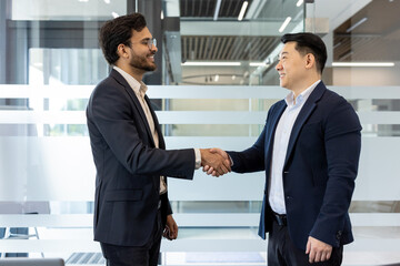 two businessmen exchange a confident handshake in modern office environment, showcasing professional